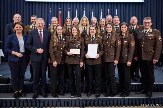 Frauen und Männer in Uniformen, eine Frau hält Urkunde, Land Oberösterreich